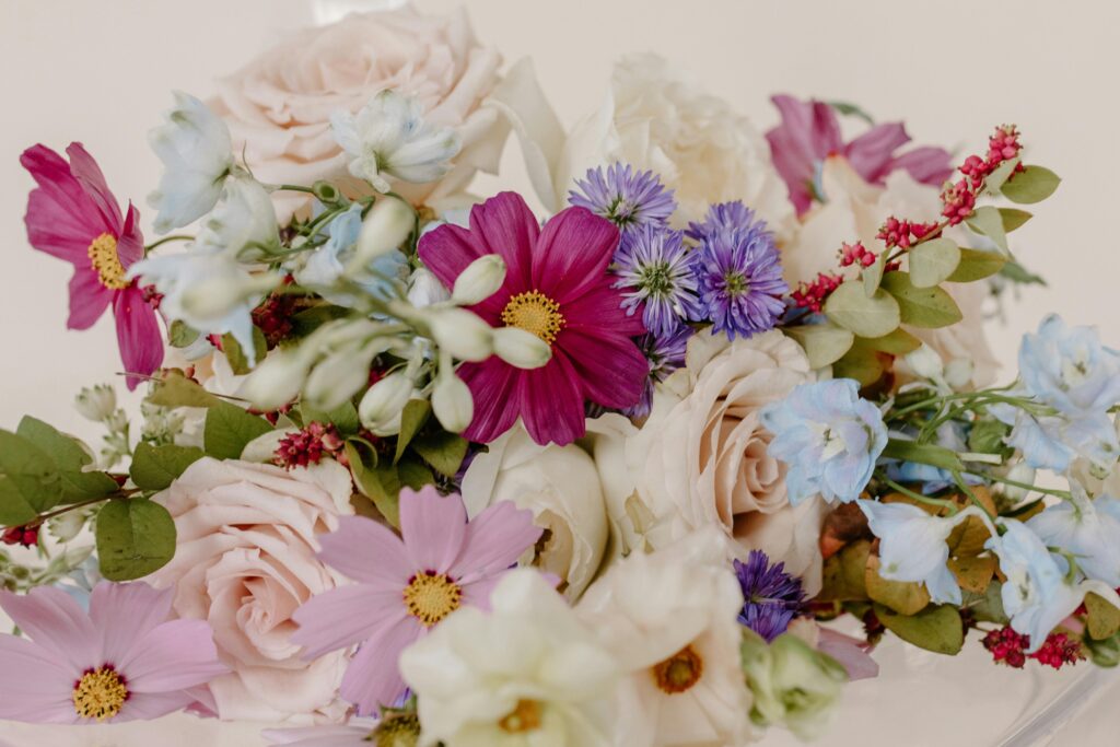 A vibrant bouquet featuring roses and various wildflowers in pink, blue, and purple hues.